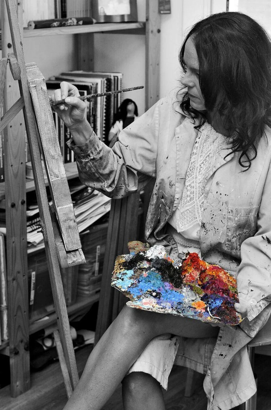Nuria Catedra pinta ante un caballete con la paleta de óleo en la mano; la fotografía es en blanco y negro y solo la paleta conserva el color.